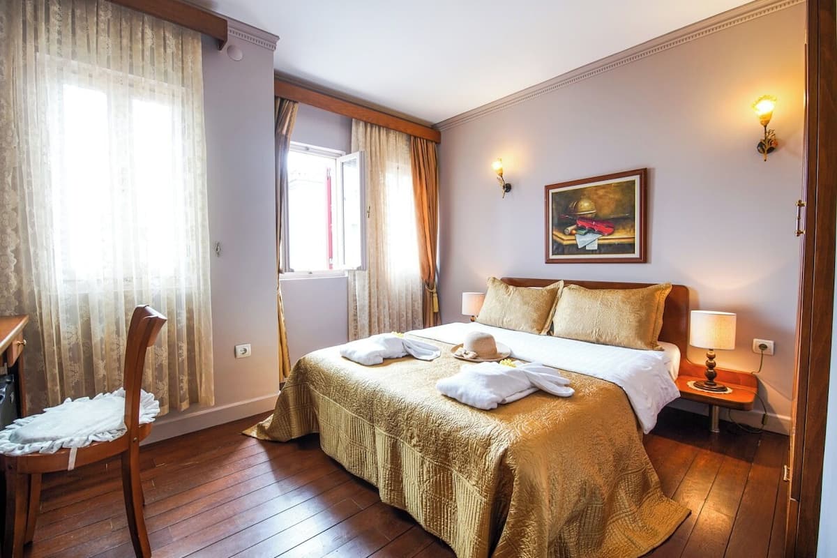 A hotel room with a large bed, a chair, a painting on the wall, and a window with curtains.
