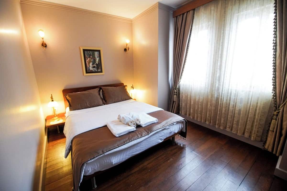 A hotel room with a large bed, two bedside lamps, a framed picture on the wall, and a window with curtains.