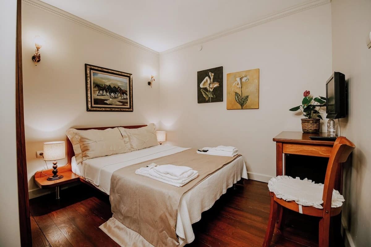A hotel room with a large bed, two bedside tables, a TV, and artwork on the walls.