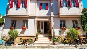 A two-story building with red shutters, a central entrance, and potted plants around the entrance.