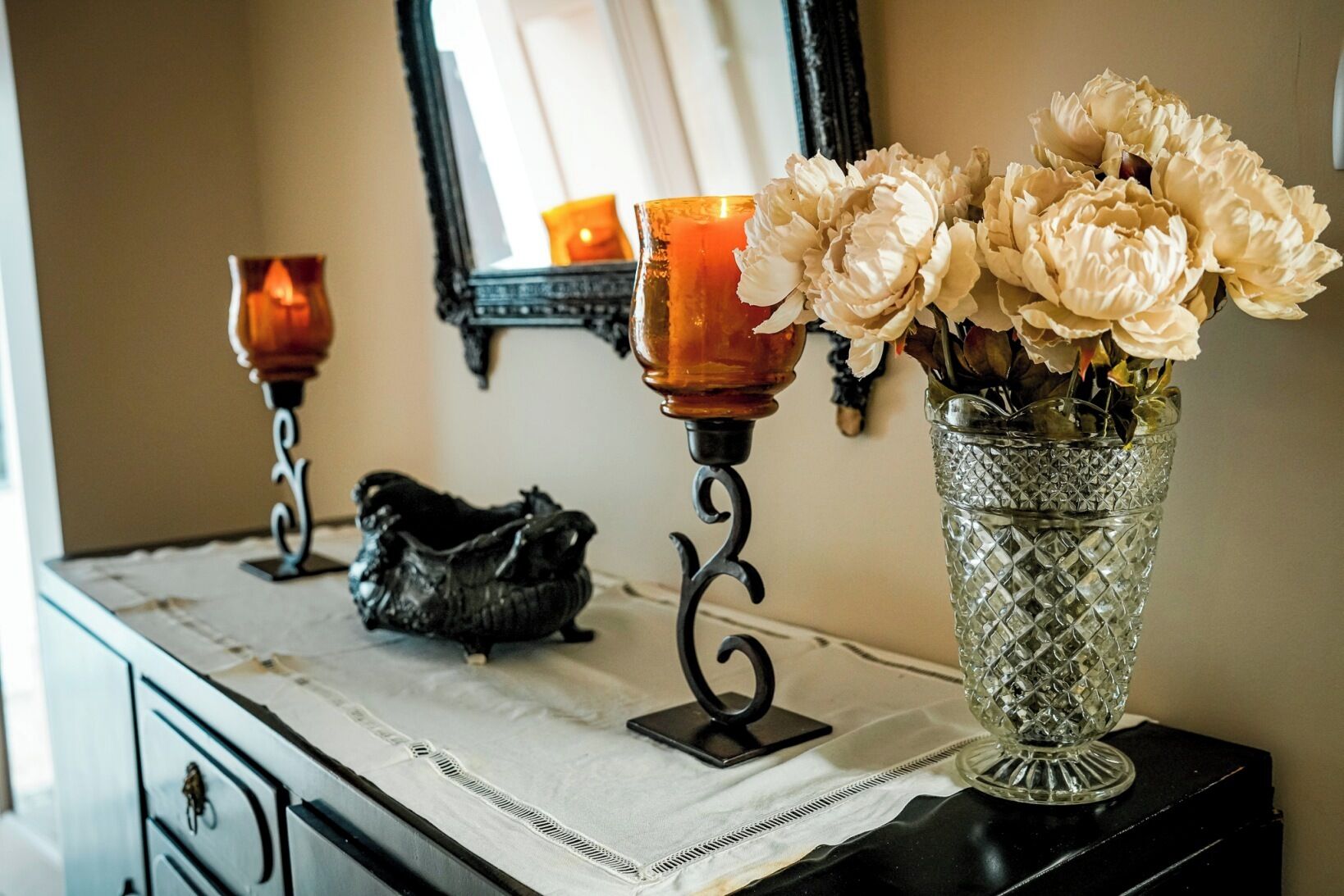 A vanity table with a vase of flowers, two candle holders, and a decorative item.