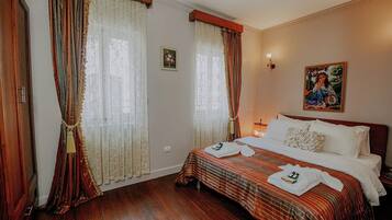 A hotel room with a large bed, two windows with curtains, a painting on the wall, and a wooden floor.