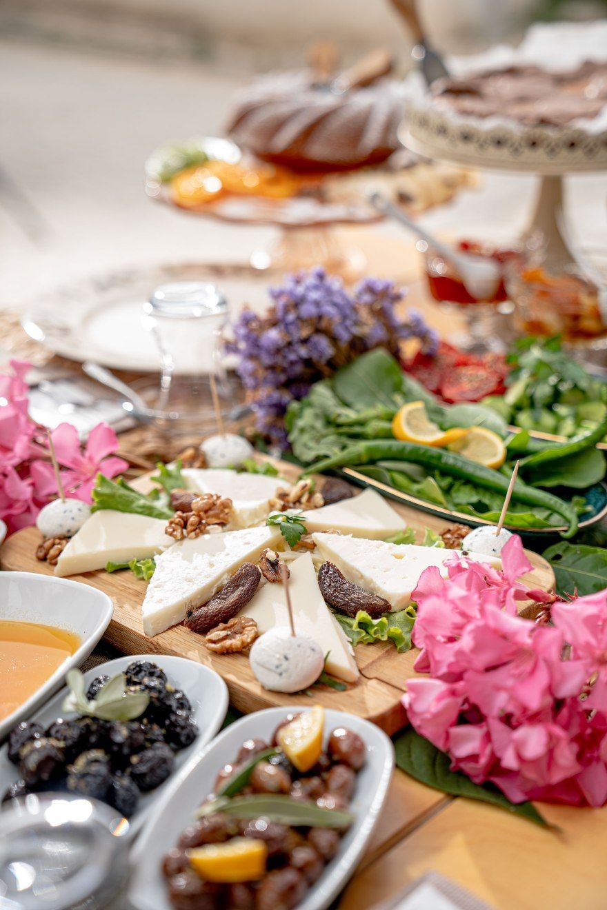 A table with various cheeses, nuts, and fruits, accompanied by flowers and a glass of wine.