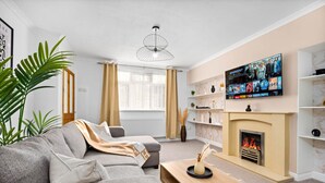 En moderne stue med en grå sofa, et træbord, en pejs og et TV ophængt på væggen.