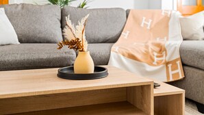 En moderne stue med en grå sofa, et træbord og en vase med tørrede planter.