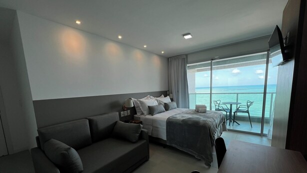A modern hotel room with a bed, a sofa, a dining table, and a balcony with a view of the sea. - RN STUDIO - APTO 1014 (Maceio)