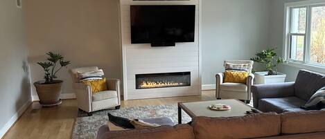 A modern living room with a fireplace, two armchairs, a sofa, and a flat-screen TV mounted above the fireplace.