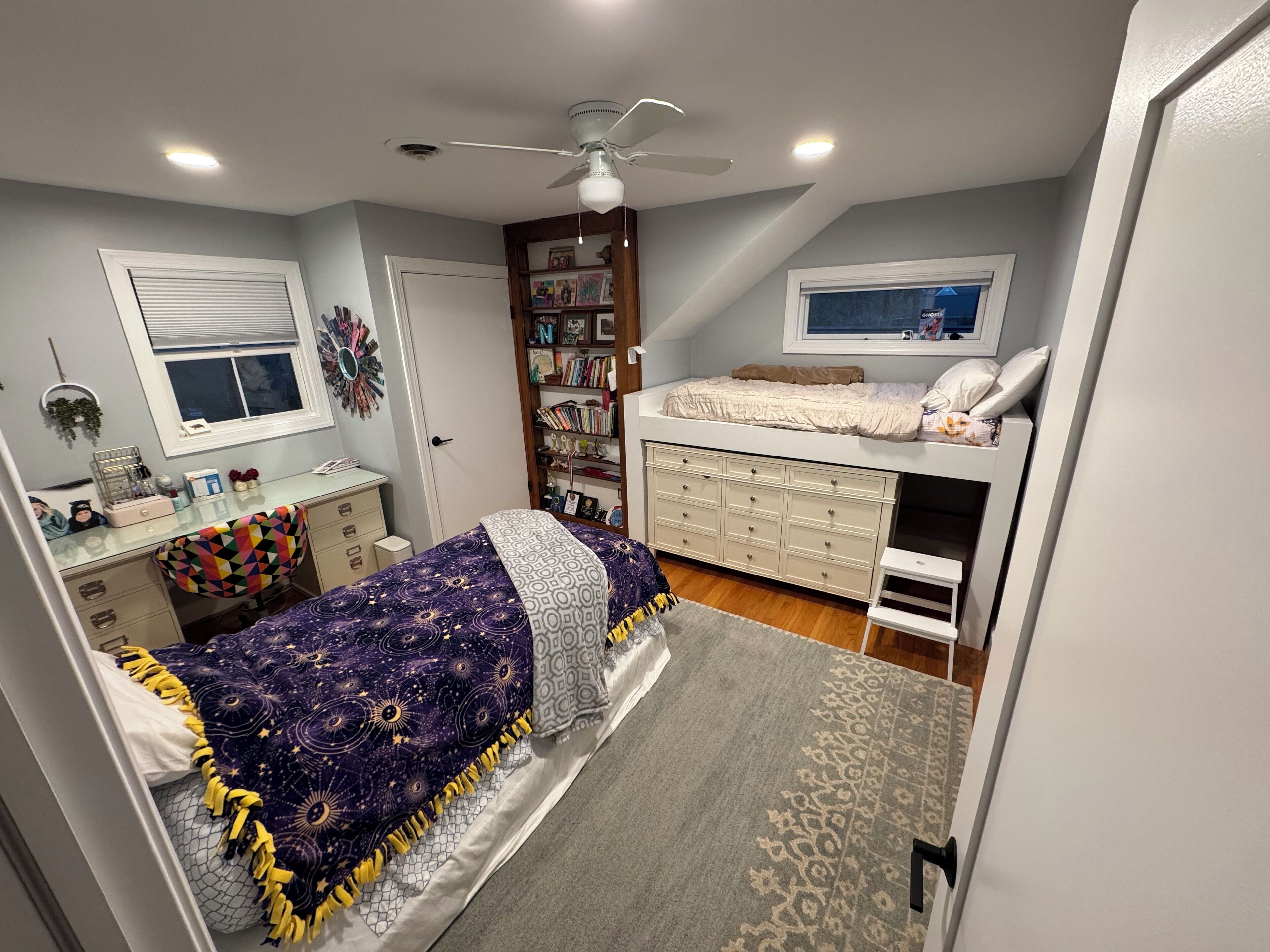 Un dormitorio con cama, escritorio, estantería y ventilador de techo.