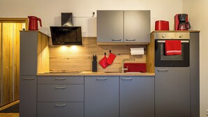 A modern kitchen with grey cabinets, a wooden countertop, a built-in oven, and a coffee maker. - Schwarzwaldmarie Titisee bathtub kitchen balcony underground parking near the lake! (Titisee-Neustadt)