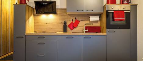 Une cuisine moderne avec des meubles gris, un plan de travail en bois, un four encastré et une machine à café.