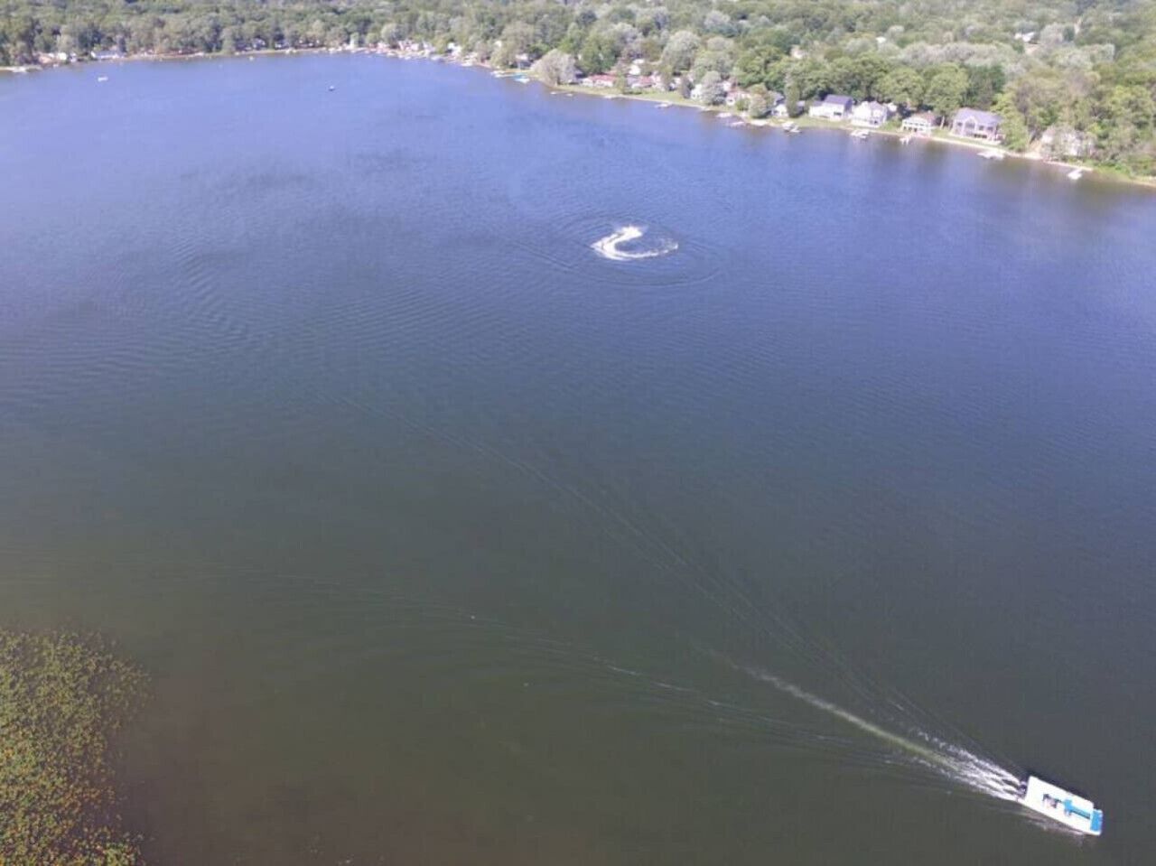 Ein großes Gewässer mit einem Boot, das eine Bugwelle hinterlässt.