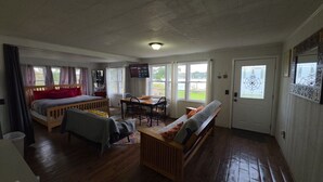 Una habitación con cama, sofá, mesa de comedor con sillas, televisión y ventanas amplias.