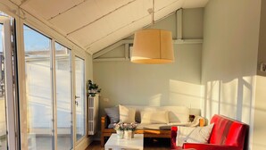 Un salón amplio con un gran ventanal, un sofá rojo, una mesa de centro blanca y una lámpara colgante.