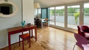 Un cuarto amplio con piso de madera, una mesa de comedor con sillas, un ventanal con vistas a la vegetación y un techo con vigas a la vista.