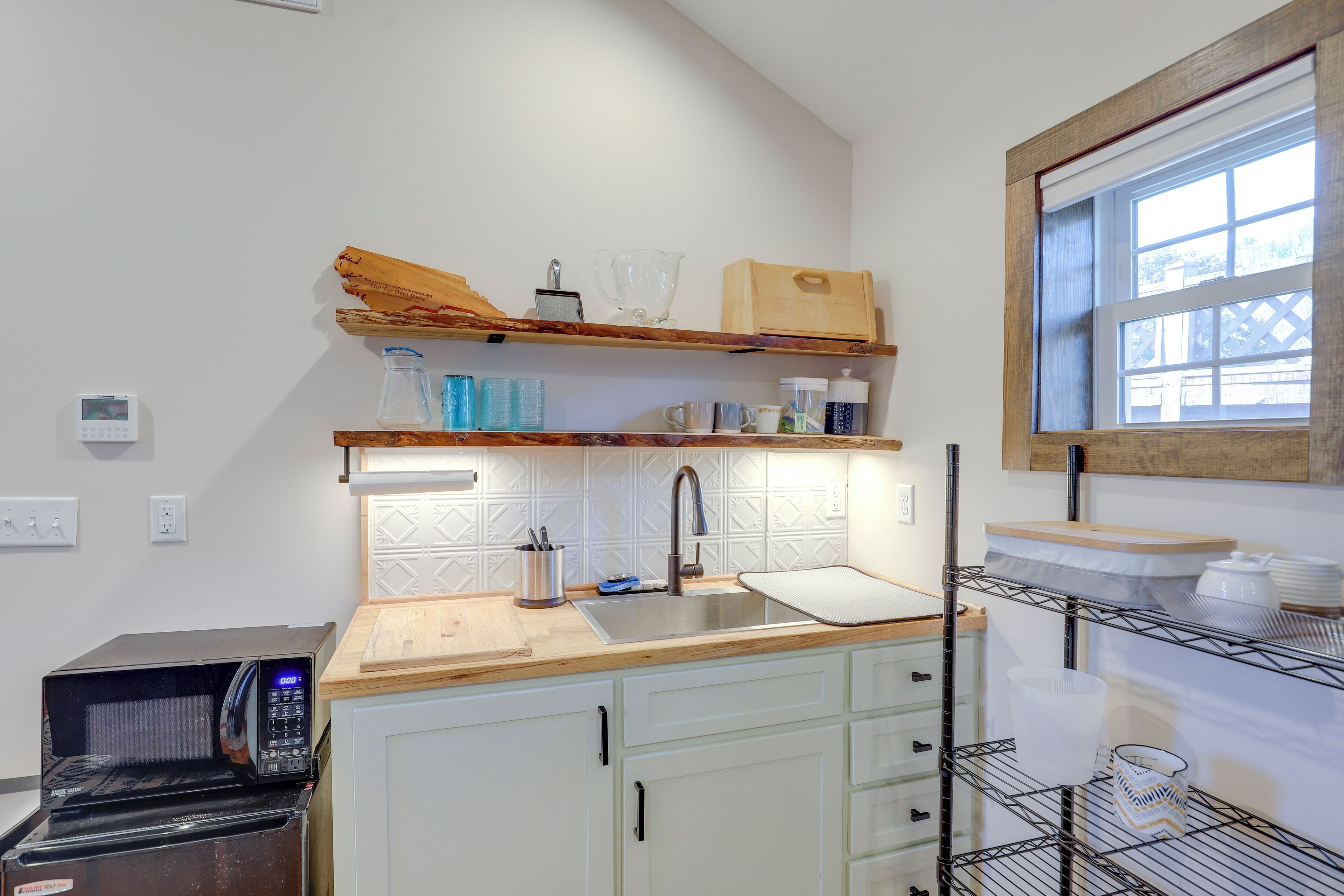 Una cocina con microondas, lavamanos, encimera de madera y estantes con utensilios de cocina.