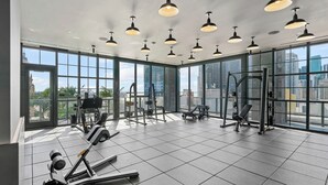 Ein Fitnessstudio mit großen Fenstern, Trainingsgeräten und Pendelleuchten.