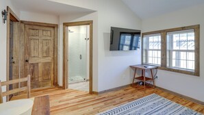 Una habitación con piso de madera, un televisor montado en la pared y una ventana con vistas al exterior.