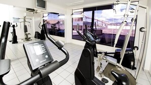Een fitnessruimte met cardioapparatuur, een televisie en grote ramen met uitzicht op een brug.