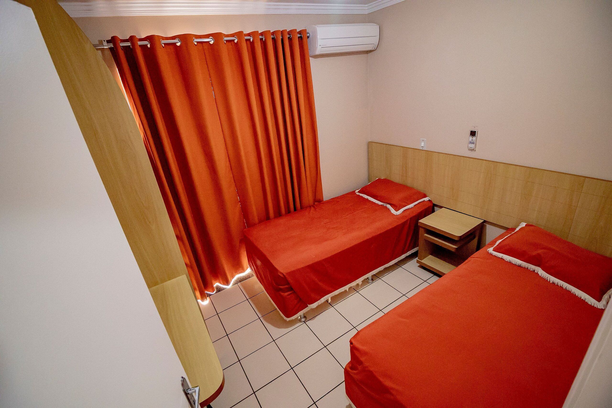 A hotel room with two beds, a wooden headboard, a small bedside table, and a curtain.
