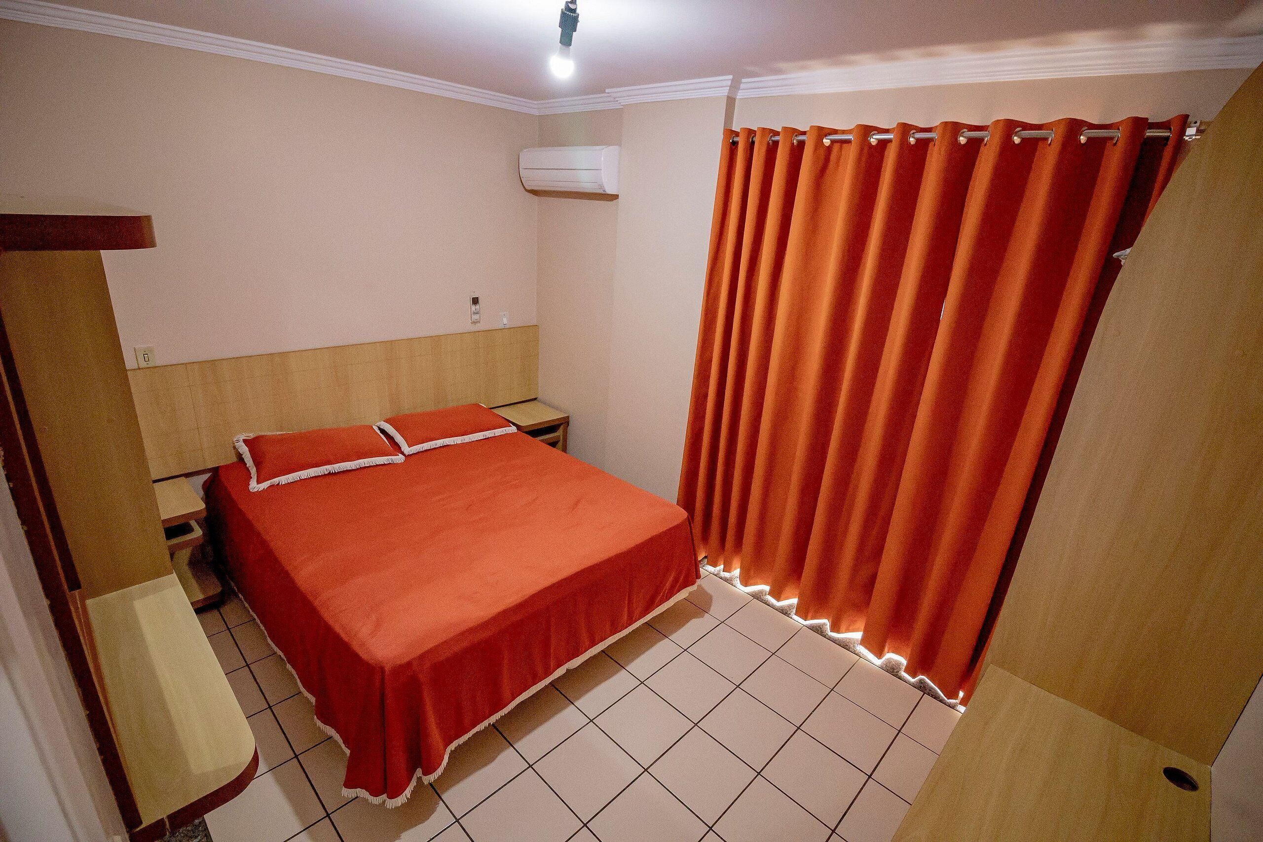 A bedroom with a bed, a nightstand, a wooden headboard, a bench, and a curtain.