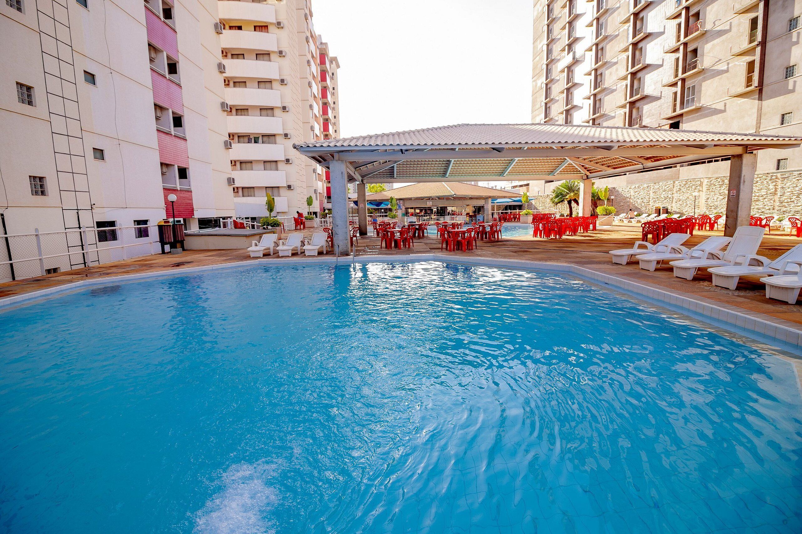 A swimming pool with lounge chairs and tables, surrounded by tall buildings.