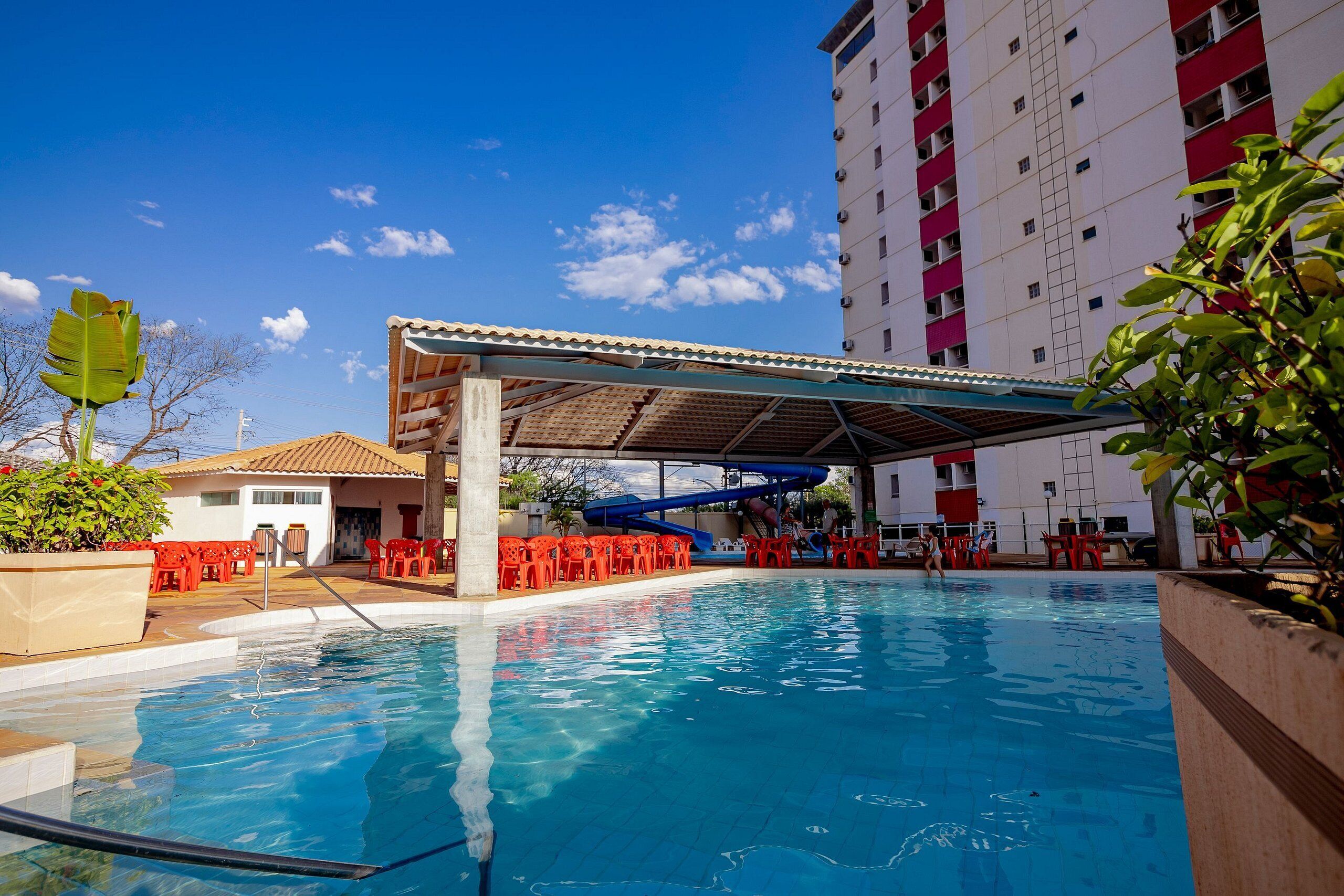 Une piscine dotée d’une zone abritée, de chaises rouges et d’un grand immeuble en arrière-plan.