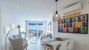 A modern living room with a dining area, a large window with a view, and a colorful wall art piece.