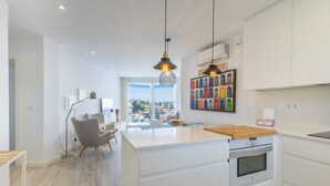A modern kitchen with a central island, white cabinetry, and a large window offering a view of the city.