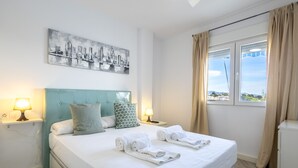 A hotel room with a bed, two bedside lamps, a cityscape painting, and a window with curtains.