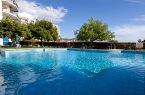 A swimming pool with clear blue water, surrounded by trees and a building with balconies. - Ref. 521865 (Nerja)
