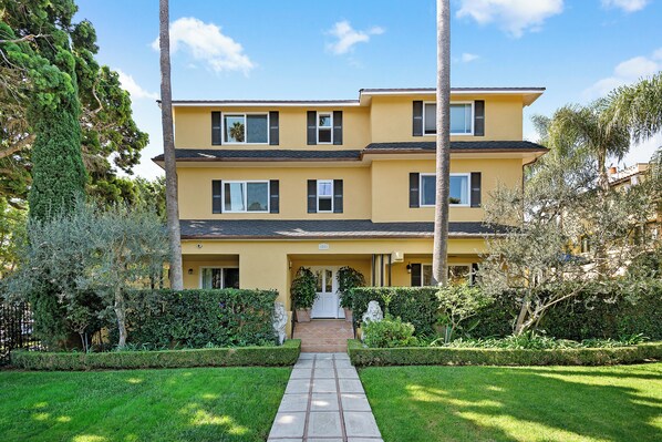 A two-story yellow building with a central entrance, surrounded by well-maintained hedges and trees. - Santa Barbara Luxury Beach Getaways (Santa Barbara)