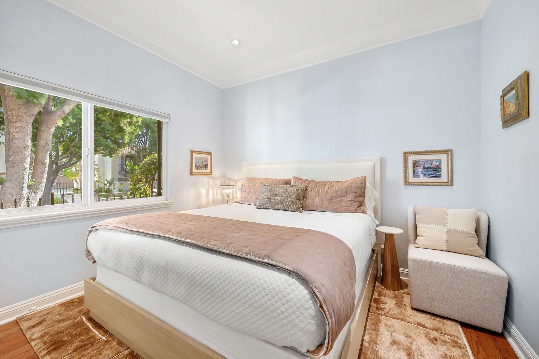 A bedroom with a large bed, a bedside table, a chair, and a window with a view of trees.