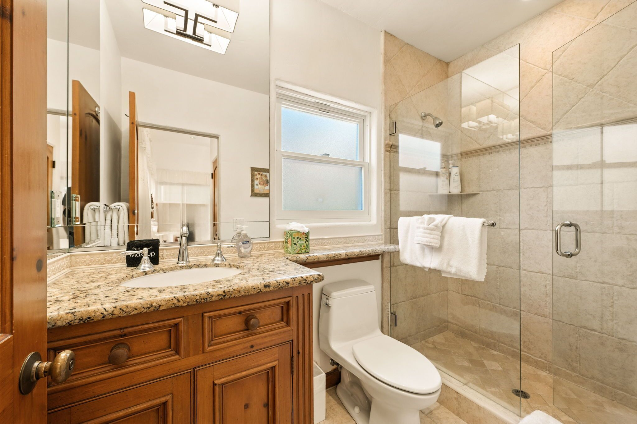 A modern bathroom with a granite countertop sink, wooden vanity, a toilet, and a glass-enclosed shower area.