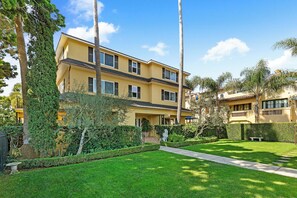A two-story yellow building with a well-maintained lawn, a stone bench, and a pathway leading to the entrance. - Santa Barbara Luxury Beach Getaways (Santa Barbara)