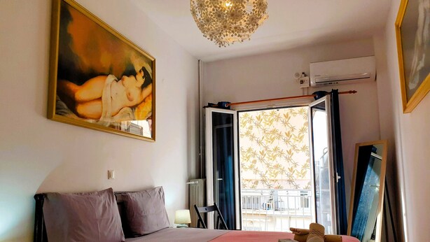 A bedroom with a bed, a painting, a chandelier, an air conditioning unit, and a view through a window. - ENTIRE APARTMENT it's everything
you need for  exceptional stay
like  your HOME (Athens)