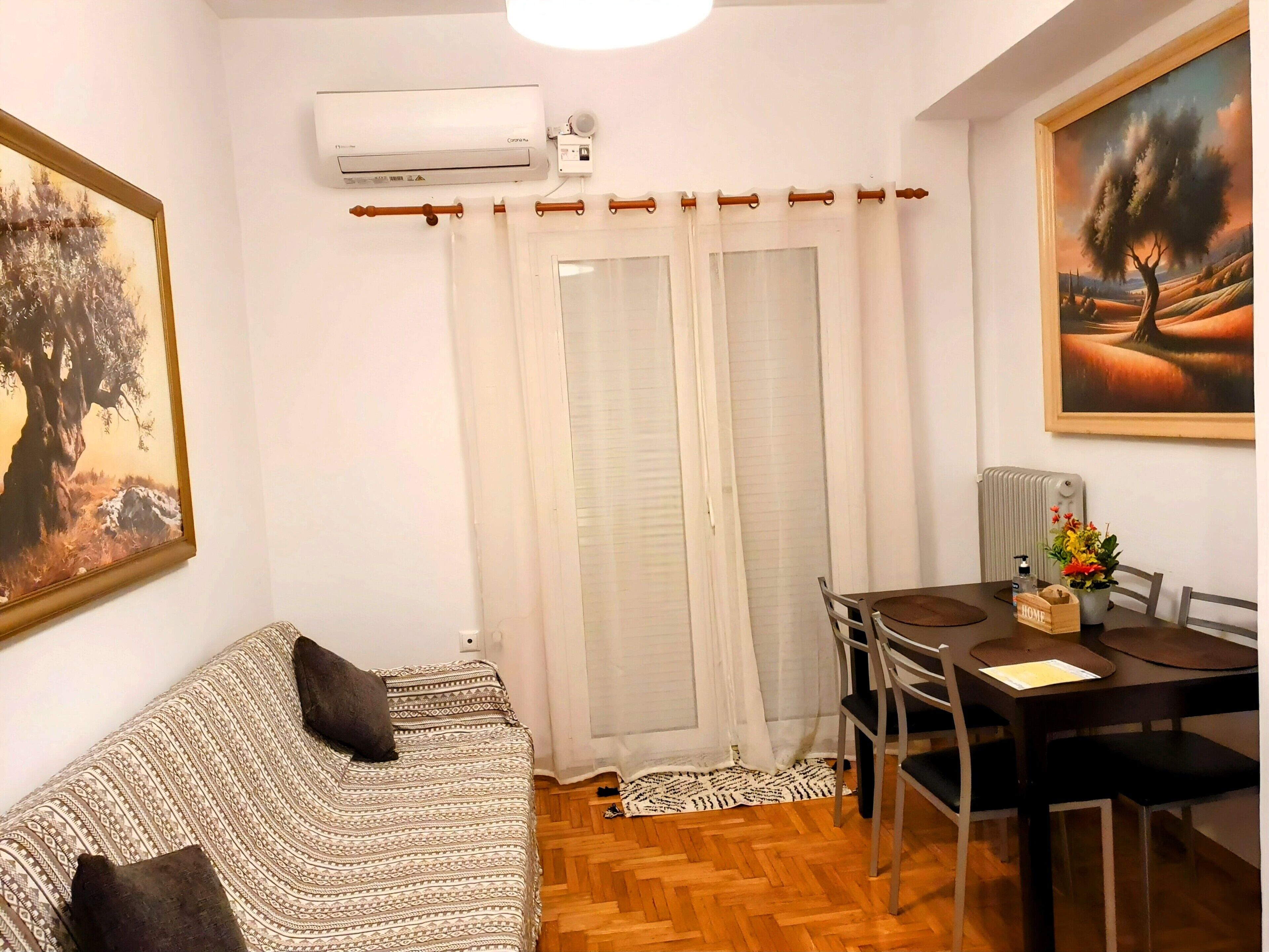 Un salon avec un canapé à motifs, une table à manger avec des chaises, un appareil de climatisation et un tableau accroché au mur.