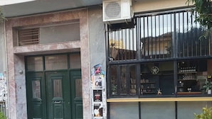 A building with a green double door, a black storefront with a window display, and an air conditioning unit above the door. - ENTIRE APARTMENT it's everything
you need for  exceptional stay
like  your HOME (Athens)