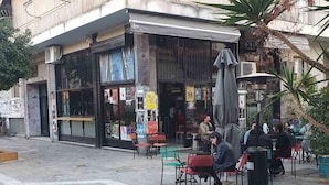 An outdoor cafe with stone flooring, outdoor seating, and a building with a black awning. - ENTIRE APARTMENT it's everything
you need for  exceptional stay
like  your HOME (Athens)