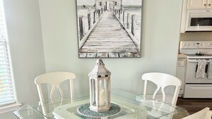 A dining area with a glass-top table, white chairs, teal cushions, and a lantern centerpiece. - Charming 3-bedroom cottage in serene Santa Rosa Beach with AC, WiFi (Santa Rosa Beach)