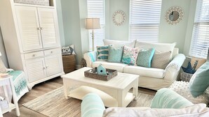 A cozy living room with a white sofa, a coffee table with a decorative basket, and a white cabinet. - Charming 3-bedroom cottage in serene Santa Rosa Beach with AC, WiFi (Santa Rosa Beach)