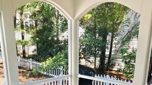 A covered patio with a table and chairs, surrounded by a white picket fence, and a view of a garden and trees. - Charming 3-bedroom cottage in serene Santa Rosa Beach with AC, WiFi (Santa Rosa Beach)