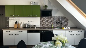 Eine moderne Küche mit grünen Schränken, einer gefliesten Spritzschutzwand und einem Essbereich mit Tisch für zwei Personen.
