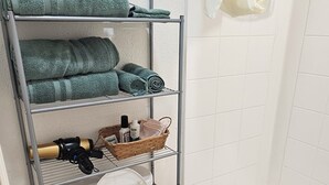 Une salle de bain avec des toilettes, une étagère avec des serviettes, un rideau de douche et une poubelle.