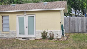 Un petit bâtiment d’un seul étage, à l’extérieur de couleur beige, avec deux portes dotées de volets verts et un petit porche.