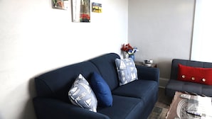 A living room with a dark blue sofa, two matching pillows, a small side table, and a vase with flowers. - Cedar Point - Sandusky Themed House (Sandusky)