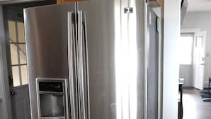 A stainless steel refrigerator with a built-in ice and water dispenser, wooden upper cabinets, and a wooden floor. - Cedar Point - Sandusky Themed House (Sandusky)