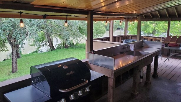 Un espace cuisine extérieur comprenant un barbecue, un évier et des tabourets de bar.