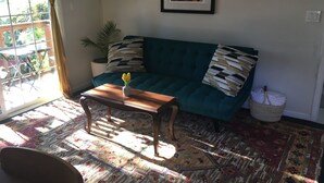 Ein Wohnzimmer mit einem blaugrünen Sofa, einem Holztisch, einem gemusterten Teppich und einem Blumentopf.