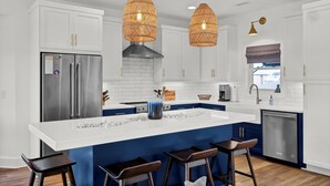 A modern kitchen with white cabinets, a stainless steel refrigerator, a blue accent wall, and pendant lights. - Waterfront 4-bedroom house on Topsail Island. Private sandbar/bring your boat! (Topsail Beach)