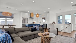 A modern living room with a sectional sofa, a glass coffee table, and a dining area with a table and chairs. - Waterfront 4-bedroom house on Topsail Island. Private sandbar/bring your boat! (Topsail Beach)